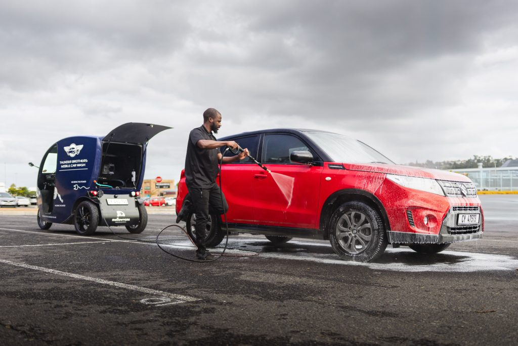 A Thunder Brothers technician pressure washing a car in a car park, with the mobile unit supplying the water alongside